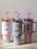 Four floral-themed Stanley tumblers on a wooden surface with a neutral background.