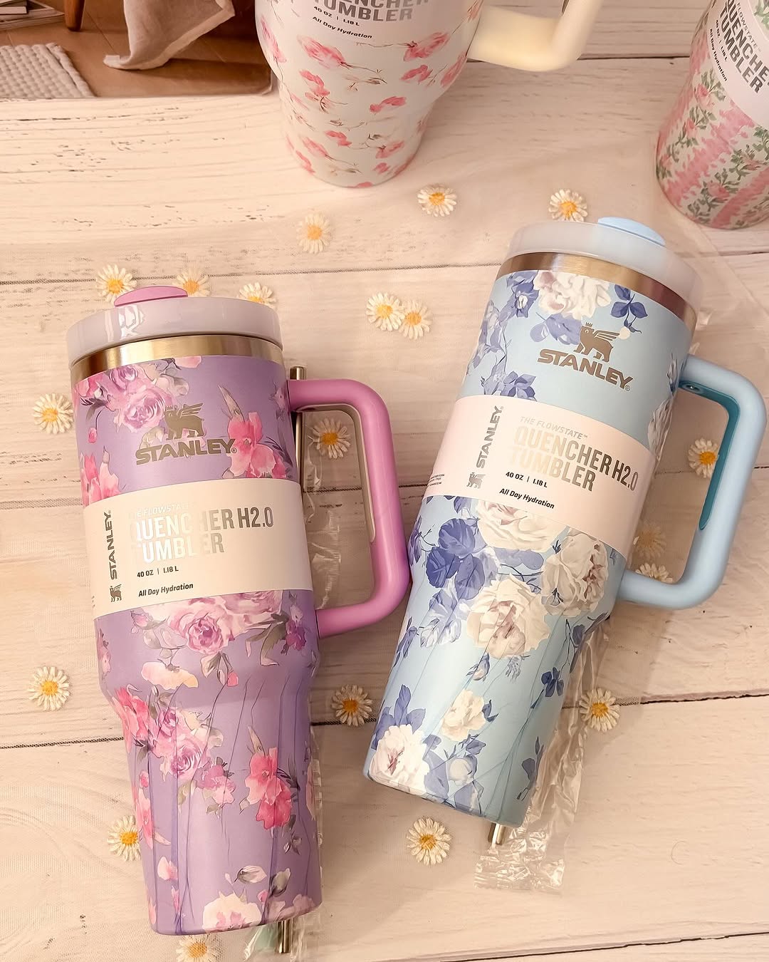 Two floral-patterned tumblers with handles on a wooden surface.