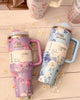 Two floral-patterned tumblers with handles on a wooden surface.