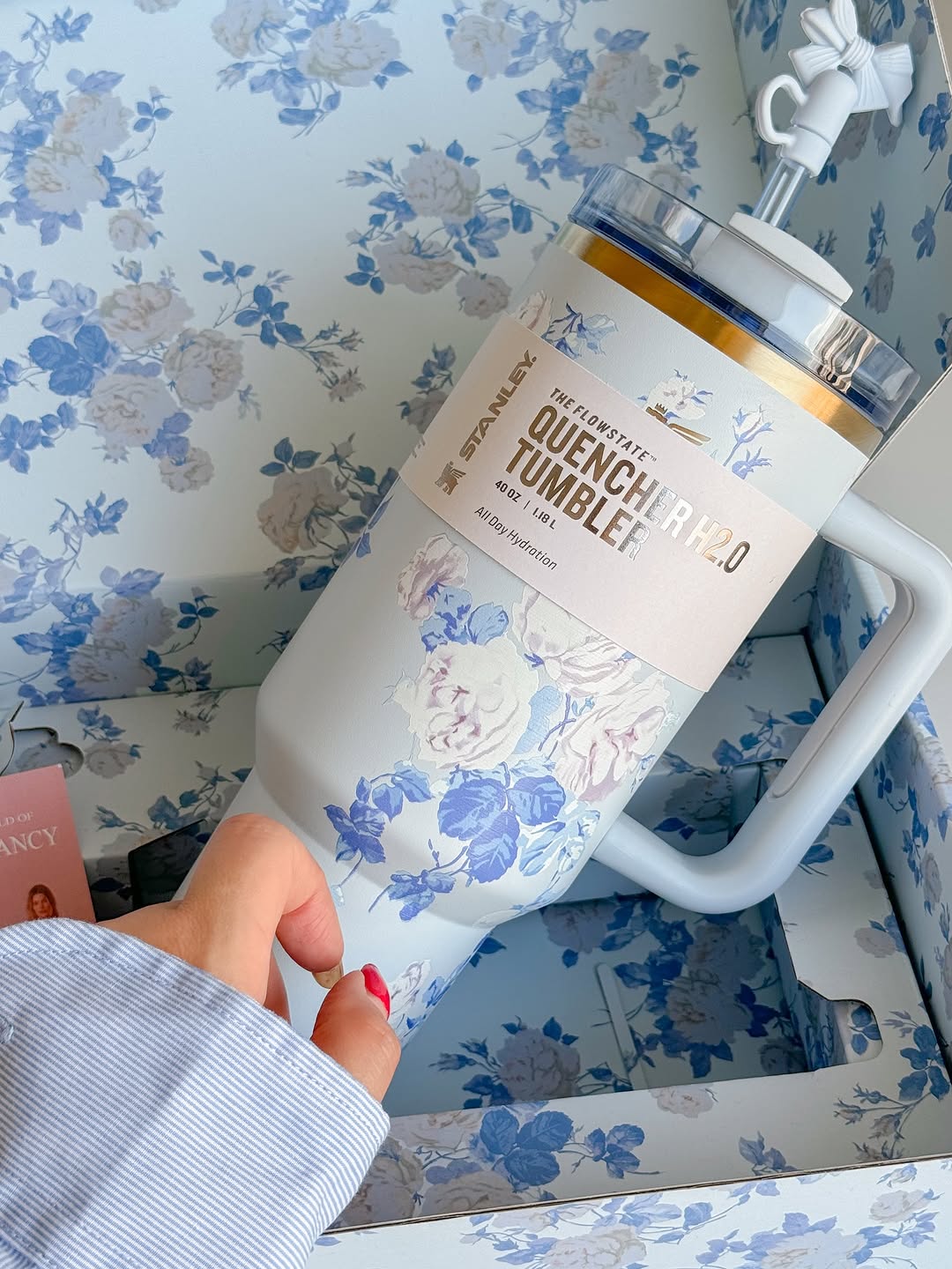 Hand holding a white tumbler with floral design against a floral-patterned background