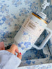 Hand holding a white tumbler with floral design against a floral-patterned background