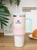 Stanley mug with pastel color pattern and reusable straw on a wooden surface with a plant in the background