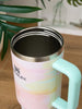 Stanley mug with pastel design and green handle on a wooden surface