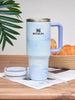 Stanley mug with gradient design on a wooden table with bread and a plant in the background