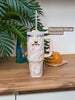 Marble-patterned tumbler with pink handle on a wooden surface, featuring a plant in the background.