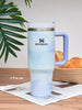 Stanley mug with gradient design on a wooden surface with a plant in the background