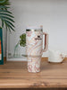Marble-patterned Stanley tumbler on a wooden surface with plants in the background