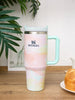Stanley mug with a pastel gradient design on a wooden surface with plants in the background