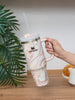 Hand holding a marbled Stanley mug with a straw on a wooden surface with a plant in the background