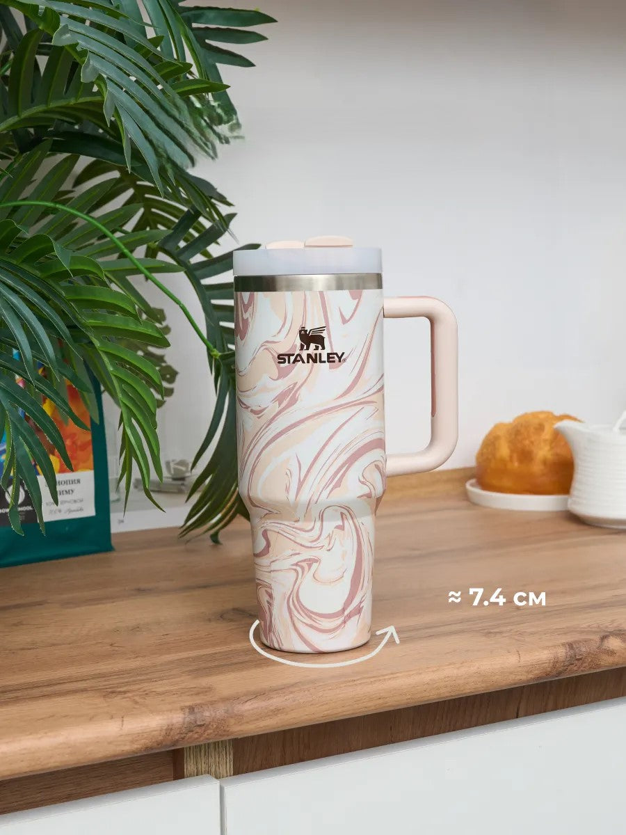 Stanley mug with marbled design on a wooden surface with a plant in the background