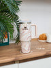 Stanley mug with marbled design on a wooden surface with a plant in the background
