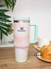 Stanley mug with a pastel design on a wooden surface with bread and a plant in the background